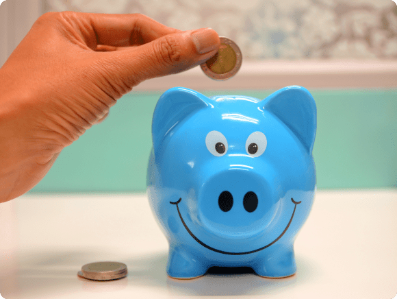 Hand putting coin in blue piggy bank.